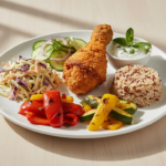 Gedeckter Teller mit frittiertem Hähnchenschenkel, Reis und Gemüse.