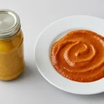 Senf im Glas links, orangefarbene Soße auf Teller rechts.