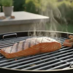 Lachssteak brutzelt auf Grillrost im Garten, Rauch steigt.