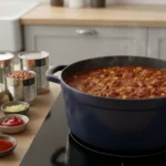 Großer Topf Chili-Eintopf kocht auf Induktionsherd; daneben Gewürze.