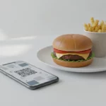 Burger, Pommes und QR-Code auf Smartphone am Tisch
