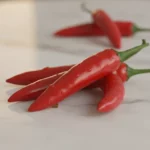 Rote Chilischoten liegen auf hellem Marmor.