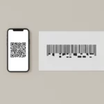 Smartphone zeigt QR-Code neben Barcode auf beigem Hintergrund.