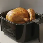 Ganzes Brathähnchen im Airfryer auf Küchenarbeitsplatte.